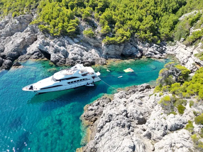 Frienship Yacht Photos Pics Luxurious Benetti Classic 115 yacht anchored in a serene, rocky cove with clear turquoise waters.