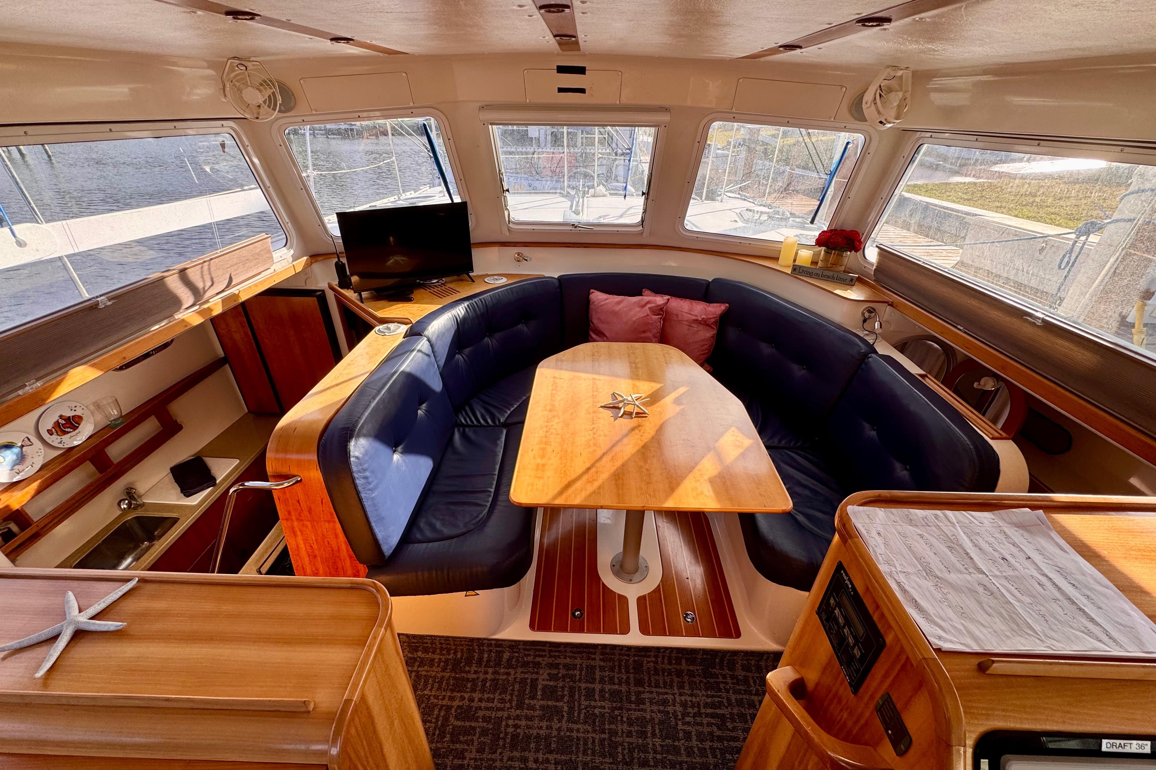 Interior of 2006 PDQ PowerCat with cozy seating, wooden table, and large windows.