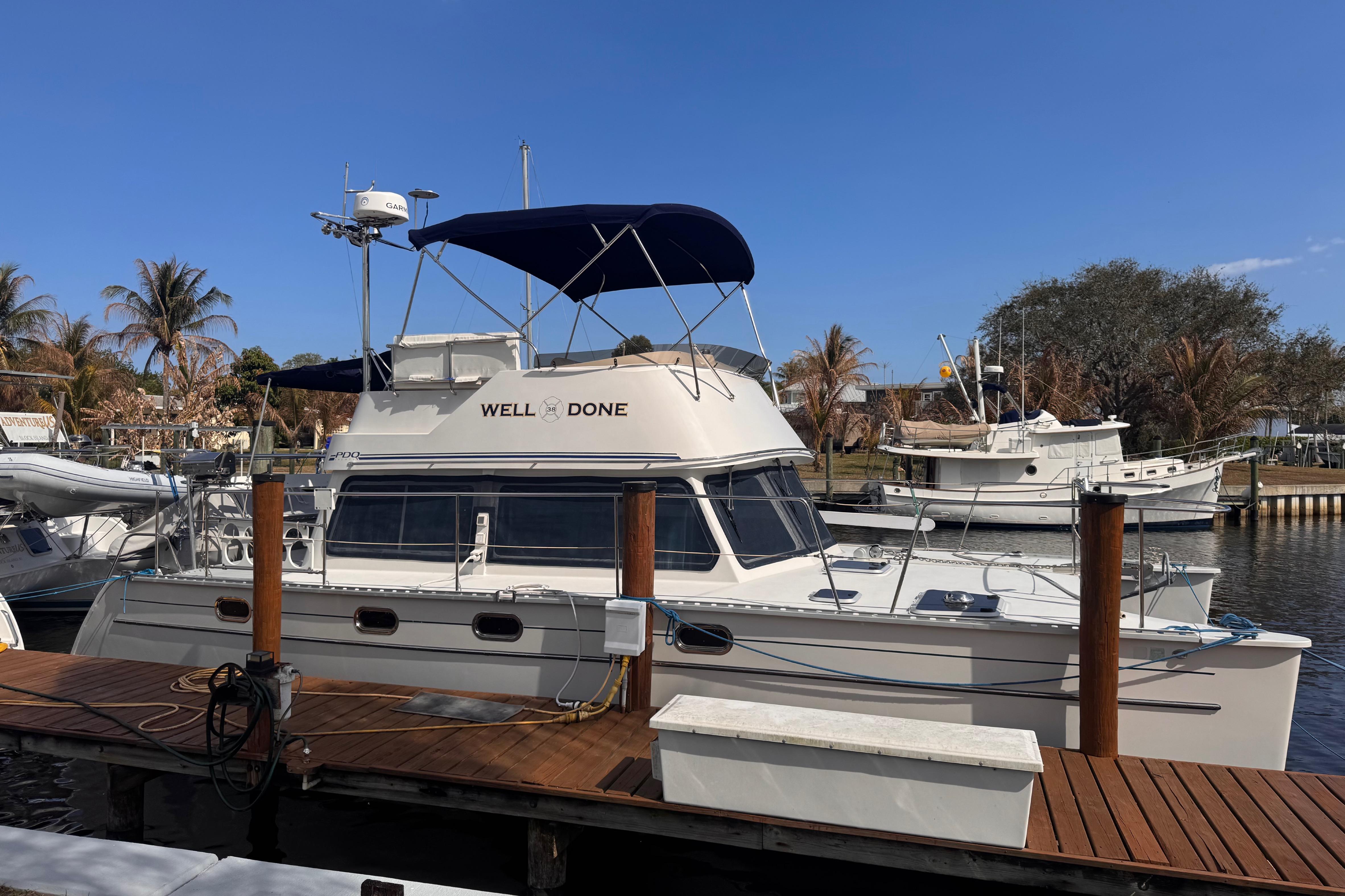 2006 PDQ PowerCat boat docked, featuring "Well Done" on the cabin, under clear blue sky.