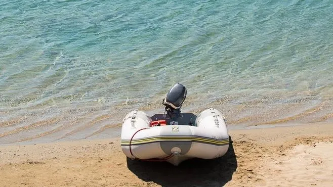 1730 Yacht Photos Pics Inflatable boat with motor on sandy beach by clear blue water.