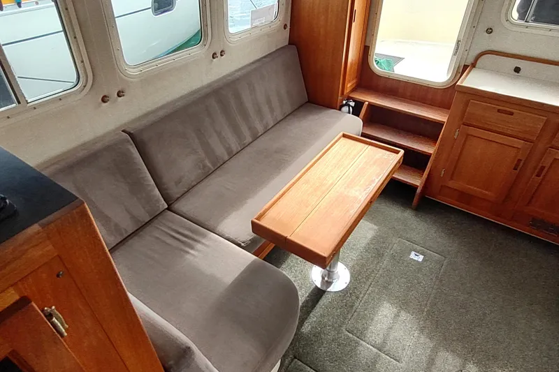 Bernardi Yacht Photos Pics Interior of 2004 Nordic Tug 32 with sofa, wooden table, and cabinetry.