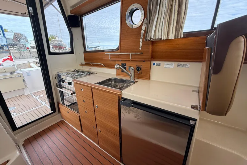  Yacht Photos Pics 2025 Ranger Tugs R-27 interior kitchen with wood cabinetry, sink, and compact appliances.