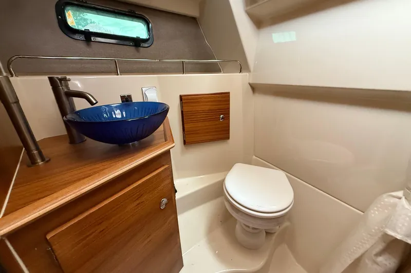  Yacht Photos Pics 2025 Ranger Tugs R-27 boat bathroom with blue glass sink and wooden cabinetry.