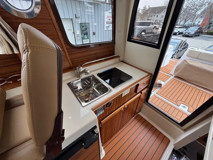  Yacht Photos Pics 2025 Ranger Tugs R-25 interior with compact kitchen, featuring sink and stove, wood finish.