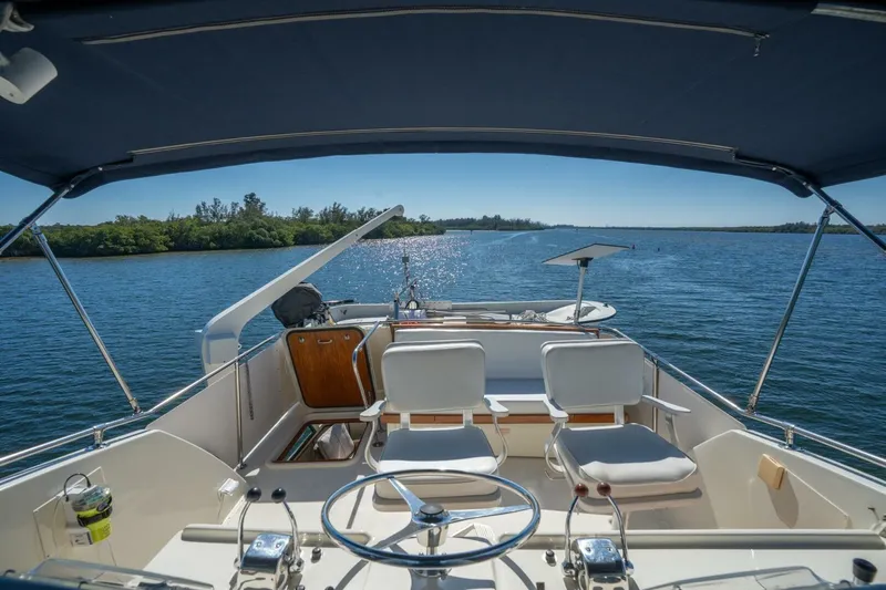 Even Keel Yacht Photos Pics 1985 Hatteras 53 Motor Yacht helm view, cruising on a serene waterway under clear skies.