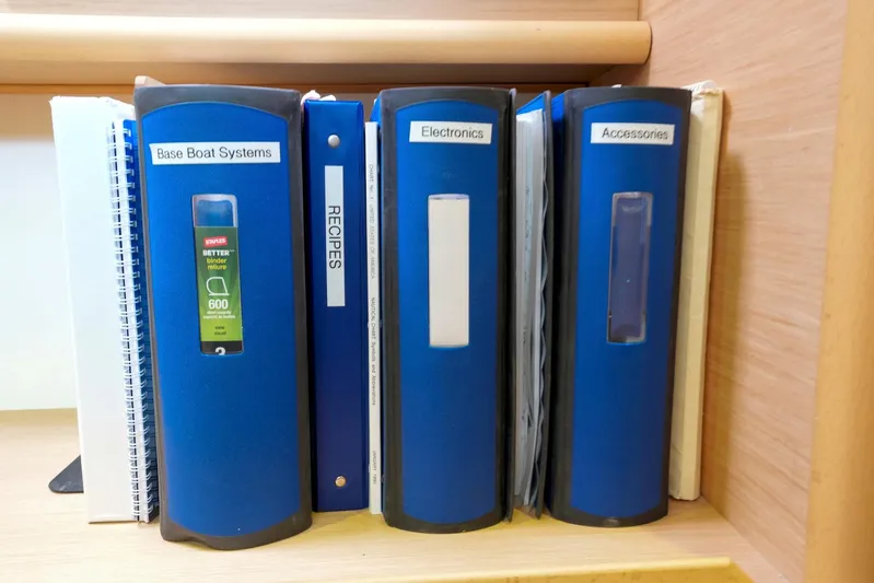 Bleu Lagoon Yacht Photos Pics Blue binders labeled "Base Boat Systems," "Electronics," and "Accessories" on a shelf.