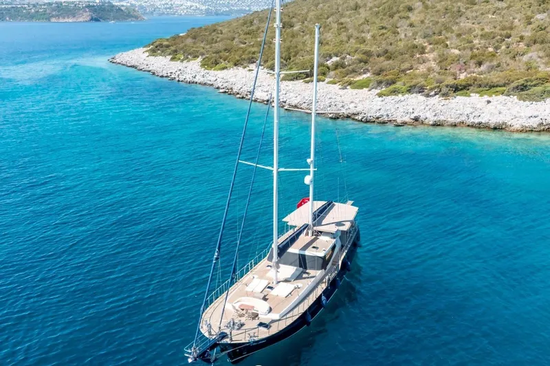 Cİca Sultan Yacht Photos Pics Luxurious Ark Yat 24M yacht sailing in clear blue waters near a rocky coastline.
