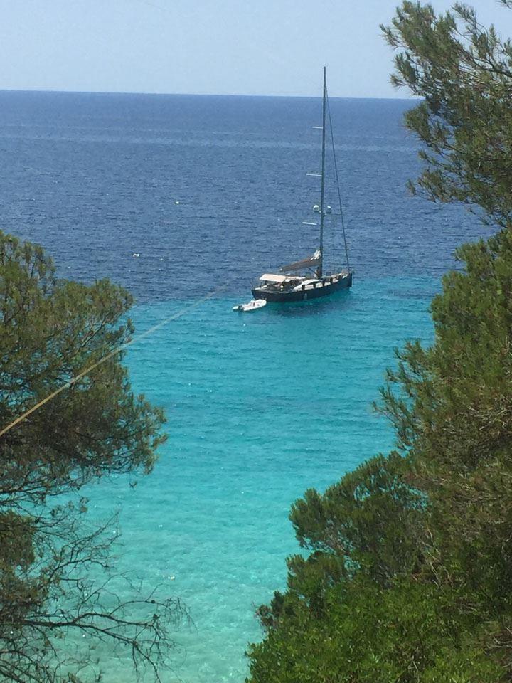 Sailboat Comar Comet 62 RS (2007) anchored in clear turquoise waters, surrounded by lush greenery.