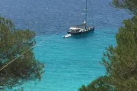Sailboat Comar Comet 62 RS (2007) anchored in clear turquoise waters, surrounded by lush greenery.