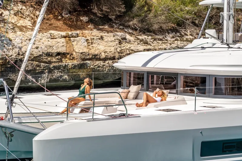  Yacht Photos Pics Luxury Lagoon 55 yacht, 2026 model, with people sunbathing on deck near rocky shoreline.