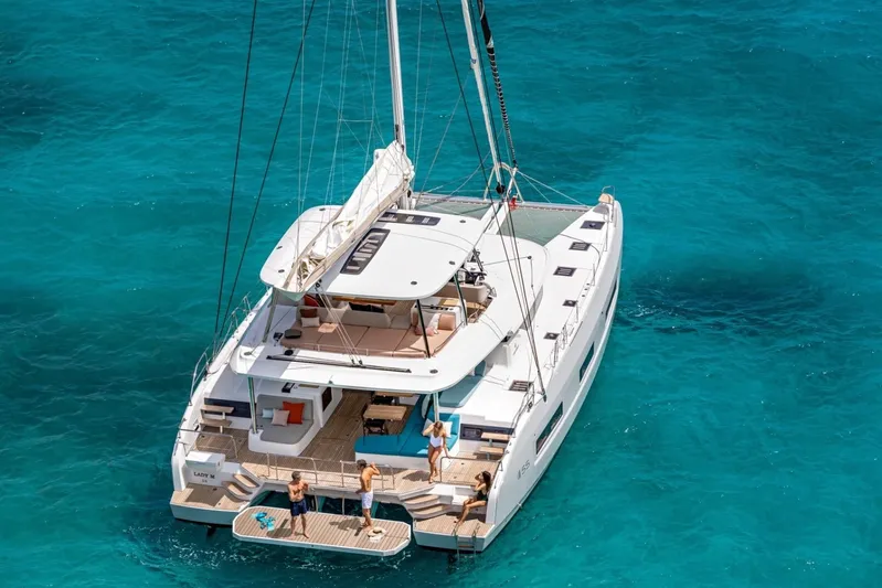  Yacht Photos Pics 2026 Lagoon 55 catamaran sailing on clear turquoise waters, with people enjoying the deck.