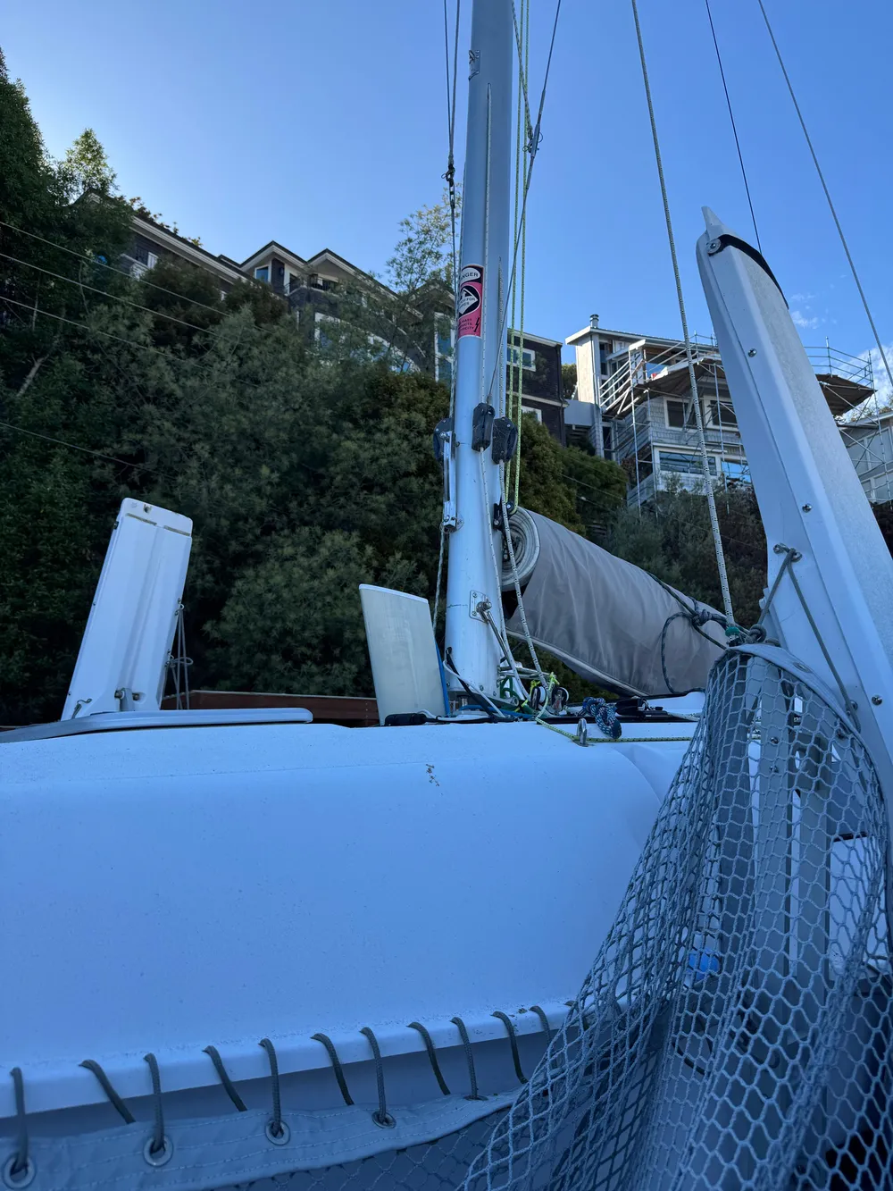 2018 Corsair 760 Sport sailboat with mast and rigging, docked near hillside homes.