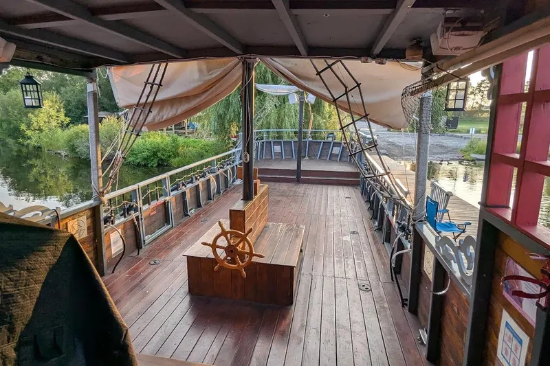  Yacht Photos Pics Custom 2016 pirate ship deck with wooden steering wheel, docked by a scenic riverbank.