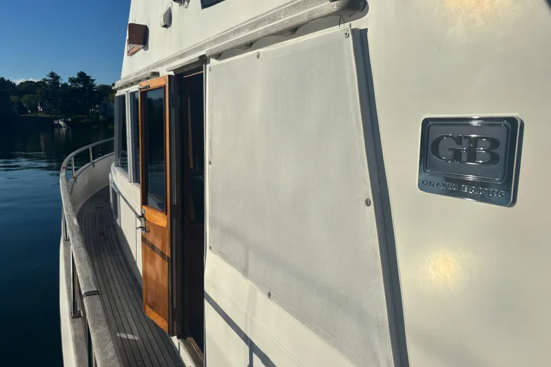 Maximon Yacht Photos Pics 1989 Grand Banks 46 Classic yacht with wooden door and GB logo on calm water.