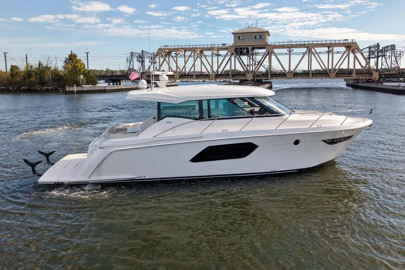  Yacht Photos Pics 2019 Tiara Yachts C49 Coupe cruising on a river with a bridge in the background.