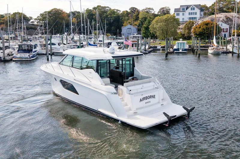  Yacht Photos Pics 2019 Tiara Yachts C49 Coupe in marina, surrounded by boats and scenic waterfront homes.