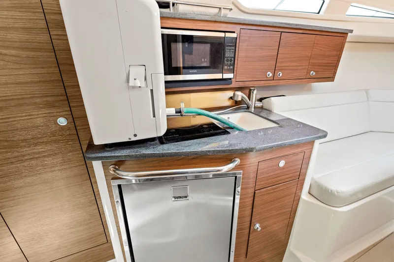  Yacht Photos Pics 2021 Boston Whaler 325 Conquest galley with microwave, sink, and wooden cabinetry.
