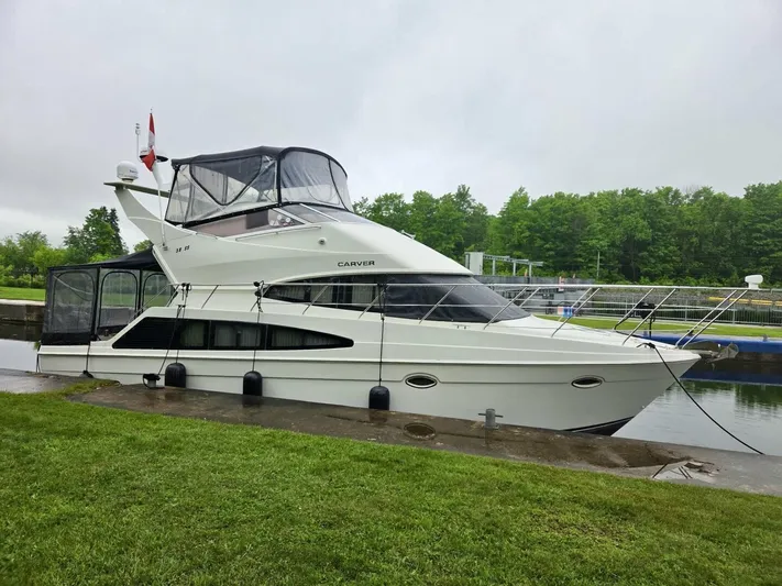  Yacht Photos Pics 2005 Carver 38 Super Sport yacht docked by a lush green shoreline.