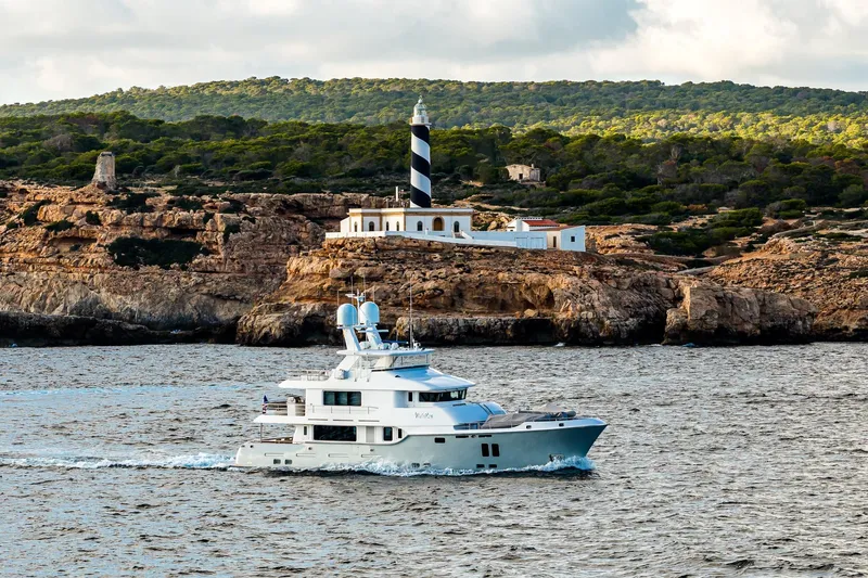  Yacht Photos Pics 2017 Nordhavn 96 yacht cruising near a rocky coastline with a lighthouse.