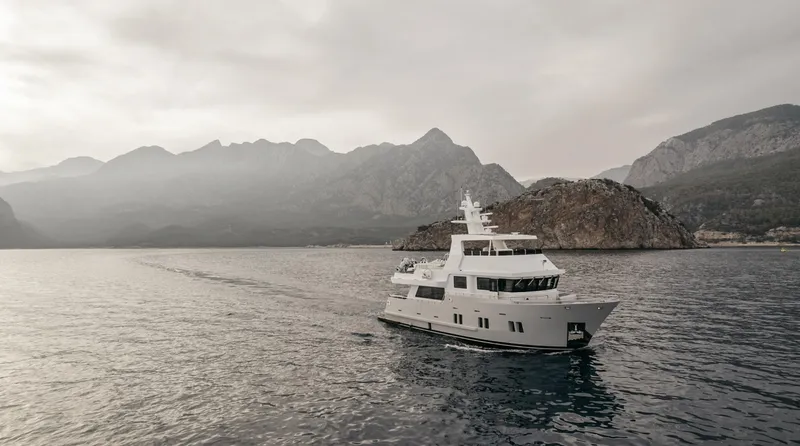 Bering 65 Explorer Yacht Yacht Photos Pics 2026 Bering 65 yacht cruising near mountainous coastline under cloudy skies.