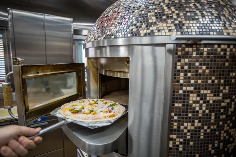 Pelorus Yacht Photos Pics Hand placing pizza into a mosaic-tiled oven, showcasing culinary preparation.