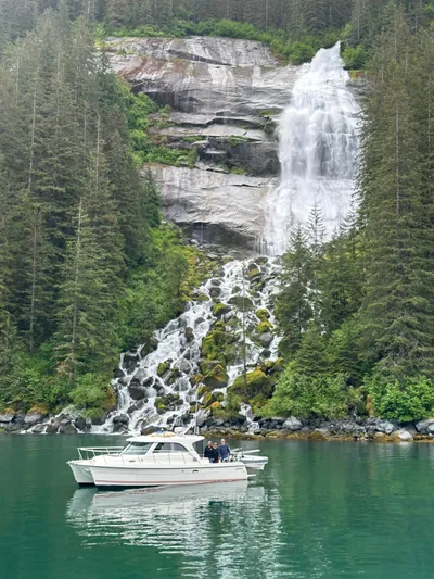  Yacht Photos Pics Boat on serene lake with waterfall backdrop, surrounded by lush forest. Aspen C100, 2026 model.