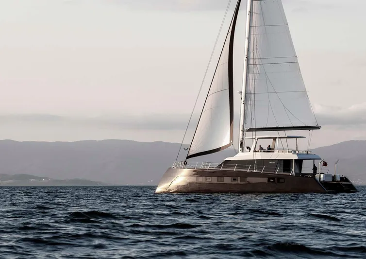 Elif Yacht Photos Pics Sailing yacht Soyaslan CAT63, 2022 model, gliding on open sea with mountains in background.