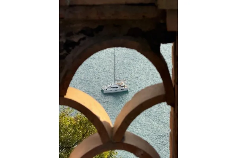 Altitude Adjustment Yacht Photos Pics Sailboat Lagoon 46 (2022) viewed through arched stone window, floating on serene blue water.