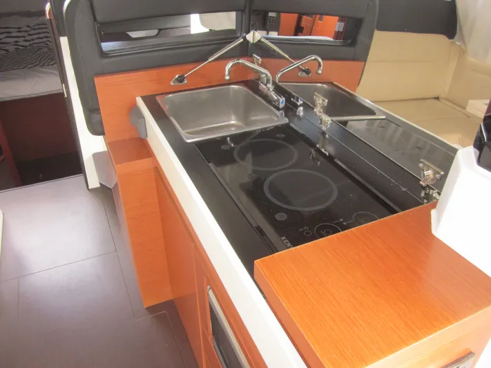  Yacht Photos Pics 2019 Jeanneau NC 33 yacht kitchen with stove, sink, and wooden cabinetry.