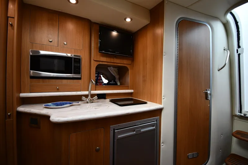  Yacht Photos Pics 2014 Rinker 310 Express Cruiser kitchen with microwave, sink, and wooden cabinetry.