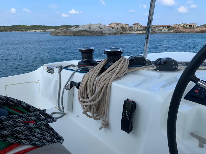 Martina Yacht Photos Pics Cockpit view of 2021 Lagoon 46 yacht with ropes and winches, near rocky shoreline.