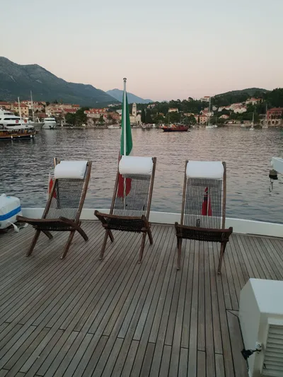  Yacht Photos Pics Three deck chairs on a yacht overlooking a serene harbor at sunset.