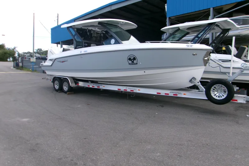  Yacht Photos Pics 2026 Monterey Elite 30 OB boat on trailer, parked outside a blue building.