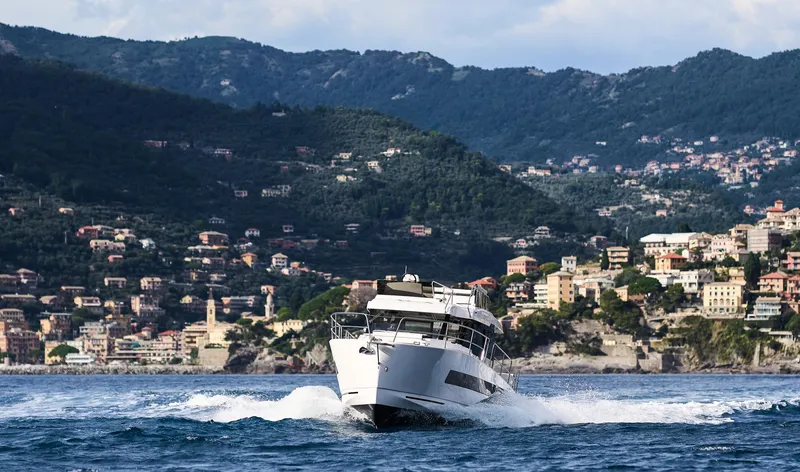  Yacht Photos Pics 2025 Northman 1300 yacht cruising near scenic coastal town with mountainous backdrop.