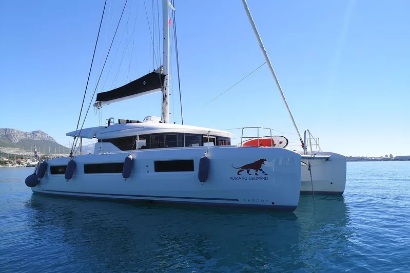  Yacht Photos Pics 2019 Lagoon 50 catamaran sailing on clear blue water, with mountains in the background.