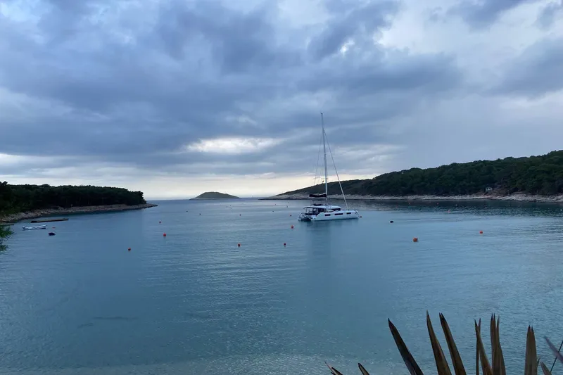 Yacht Photos Pics Sailboat Lagoon 50 (2019) anchored in a serene bay under cloudy skies.
