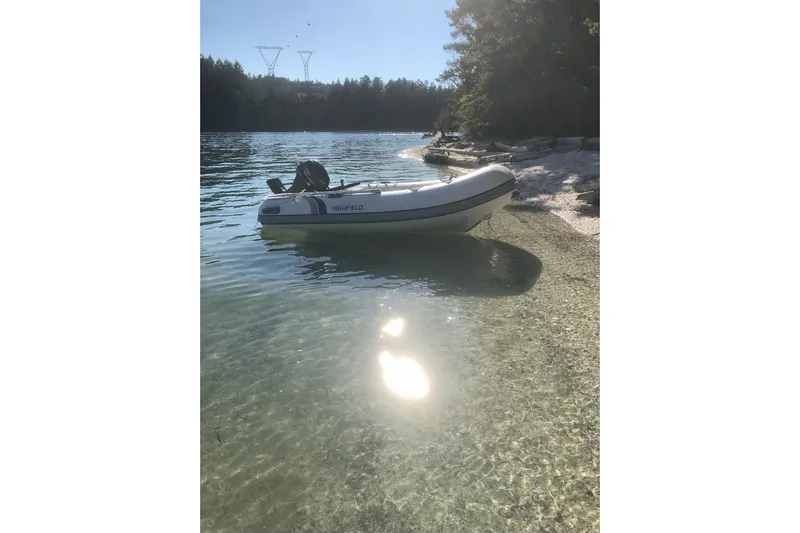 Kindred Spirit Yacht Photos Pics Inflatable boat on clear water near a forested shoreline, sunny day.