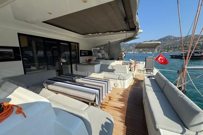  Yacht Photos Pics Luxurious 2021 Excess 15 yacht deck with seating, table, and Turkish flag, docked in scenic harbor.