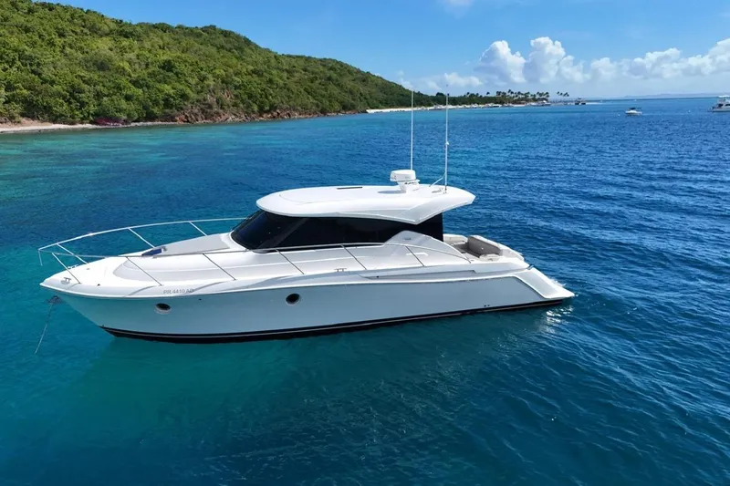  Yacht Photos Pics 2022 Tiara Yachts C39 Coupe cruising in clear blue waters near a lush green island.