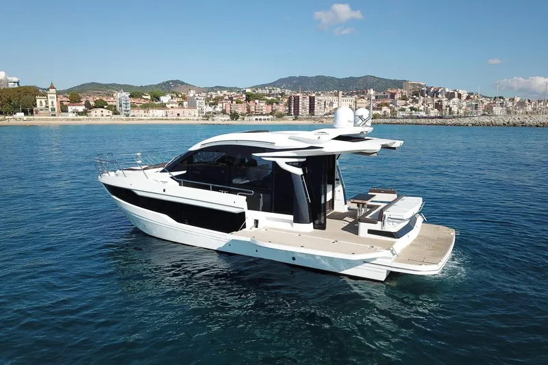  Yacht Photos Pics 2024 Galeon 410 HTC yacht cruising near a scenic coastal city backdrop.