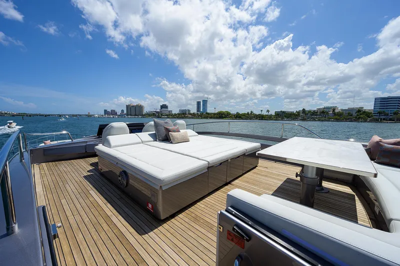 Shine Yacht Photos Pics Luxurious 2022 Pershing 9X yacht deck with sun loungers and table, overlooking scenic waterfront.