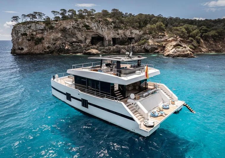 Rosa Del Mar Yacht Photos Pics Luxurious 2017 Sunreef Supreme 68 yacht anchored in clear blue waters near rocky coastline.