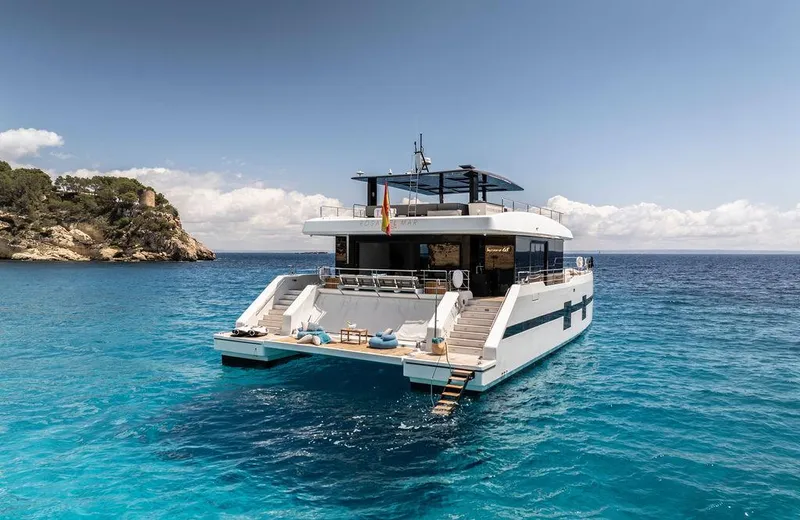 Rosa Del Mar Yacht Photos Pics Sunreef Supreme 68 yacht, 2017 model, anchored in clear blue waters near a rocky coastline.