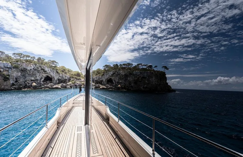 Rosa Del Mar Yacht Photos Pics Sunreef Supreme 68 yacht cruising near rocky coastline under a partly cloudy sky.