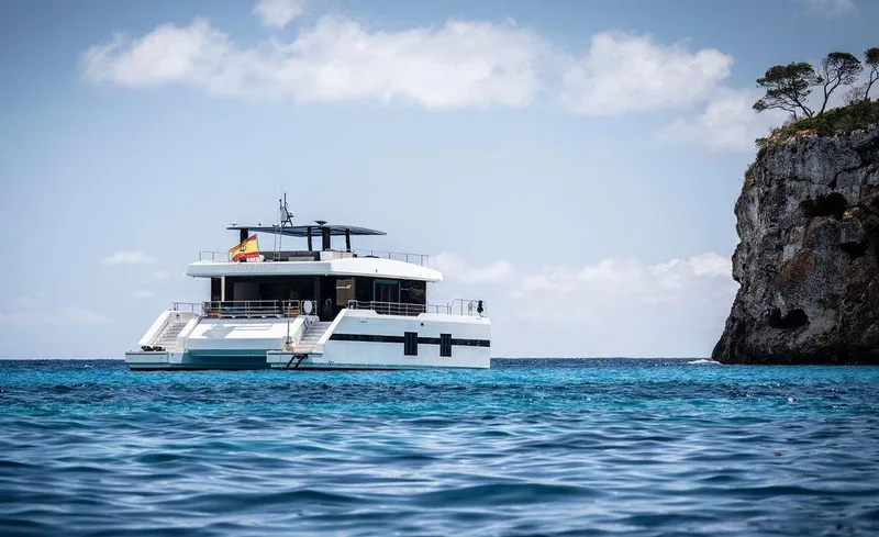 Rosa Del Mar Yacht Photos Pics Luxurious 2017 Sunreef Supreme 68 yacht anchored near a rocky coastline.