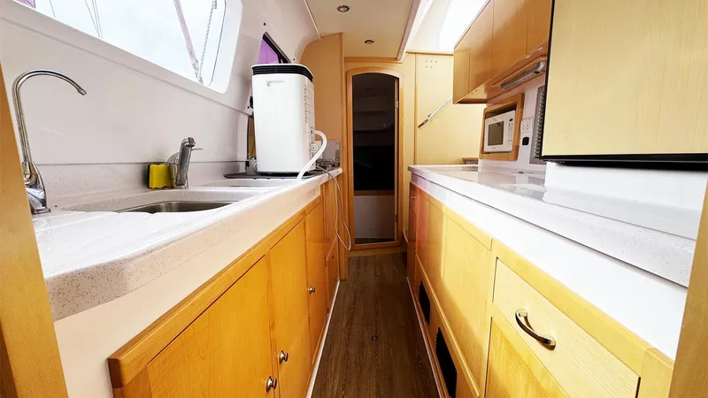 Honu Kai Yacht Photos Pics 2019 Seawind 1260 yacht kitchen with wooden cabinets, modern appliances, and sleek countertops.