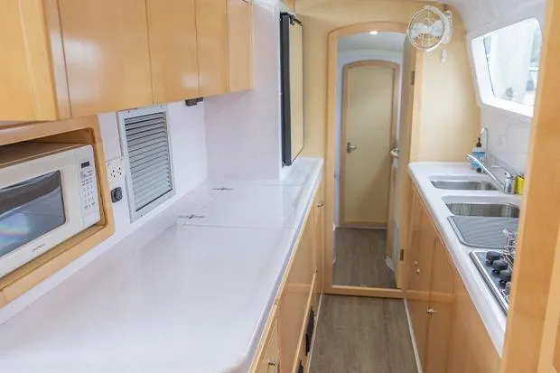 Honu Kai Yacht Photos Pics 2019 Seawind 1260 yacht interior kitchen with wooden cabinets, microwave, and dual sinks.