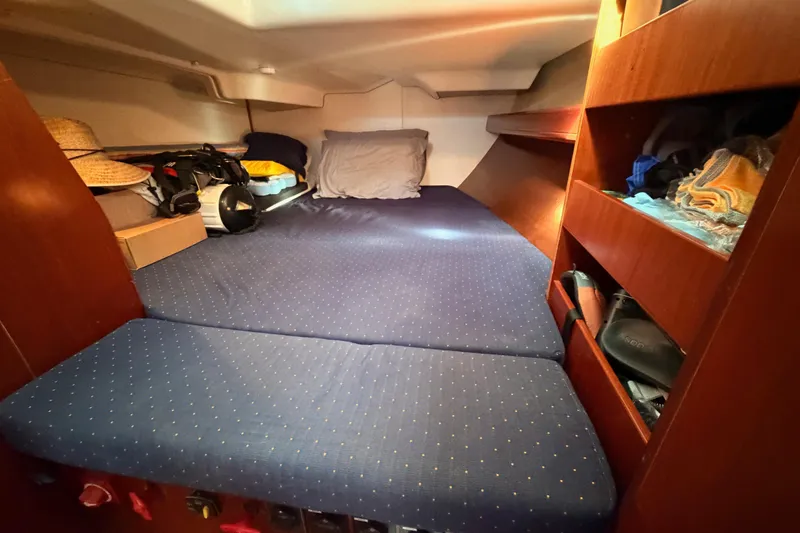 Tadpole Yacht Photos Pics Cozy cabin interior of 2005 Beneteau Oceanis Clipper 423 with blue bedding and wooden shelves.