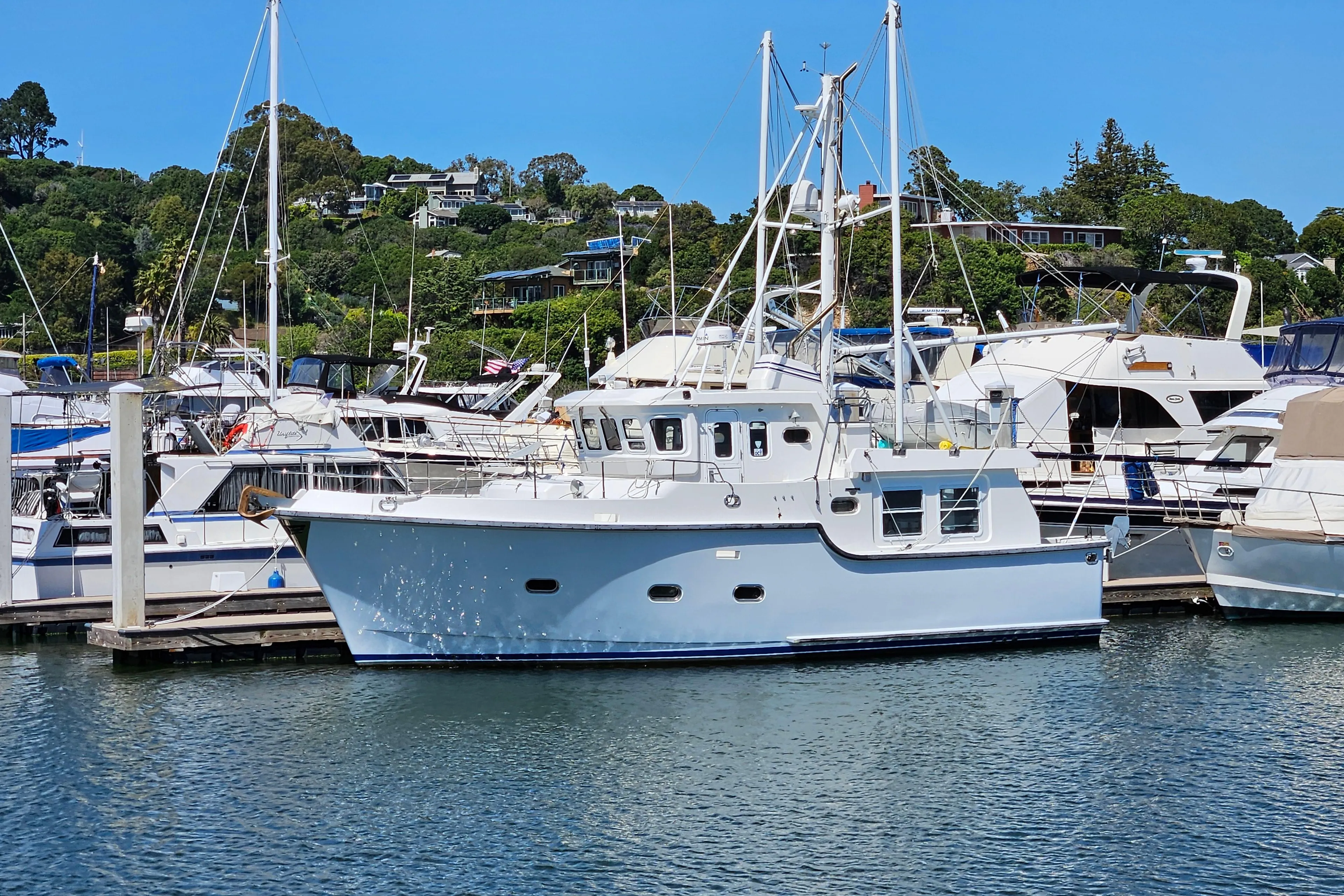 2002 Nordhavn Trawler docked in a marina, surrounded by other boats, under a clear blue sky.
