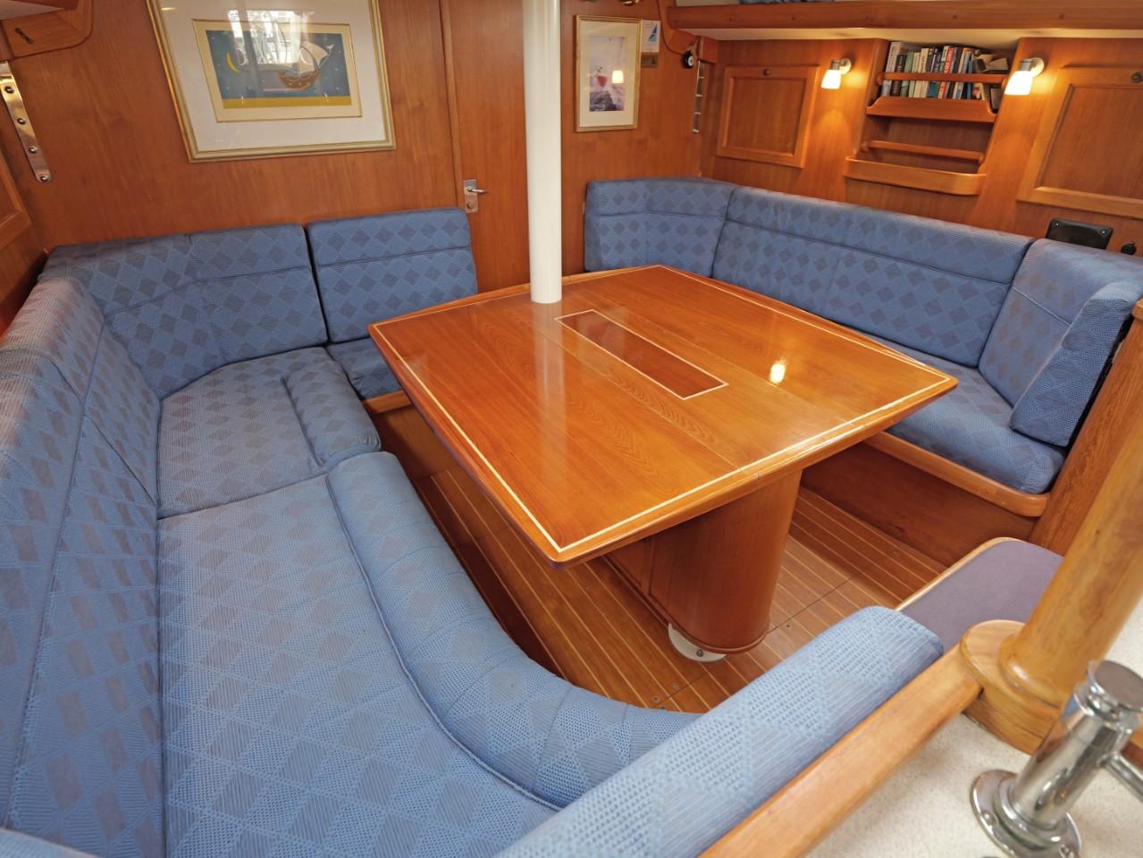 Luxurious 1999 Rustler 42 yacht interior with wooden table and blue cushioned seating.